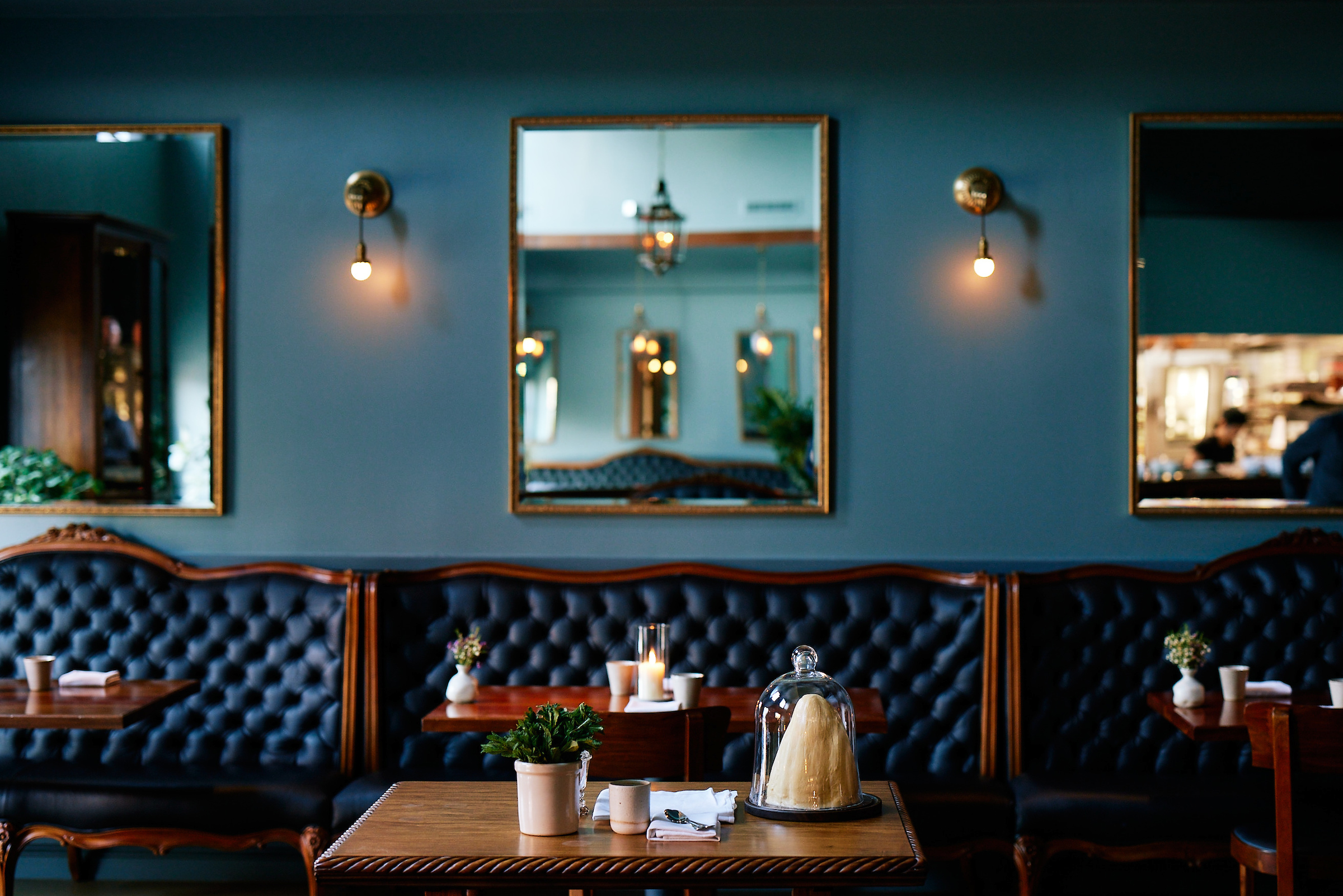 MANZKE Interior 1 shot of wooden tables and tufted navy blue leather banquettes in the manzke dining room, which is painted in a medium blue-green hue