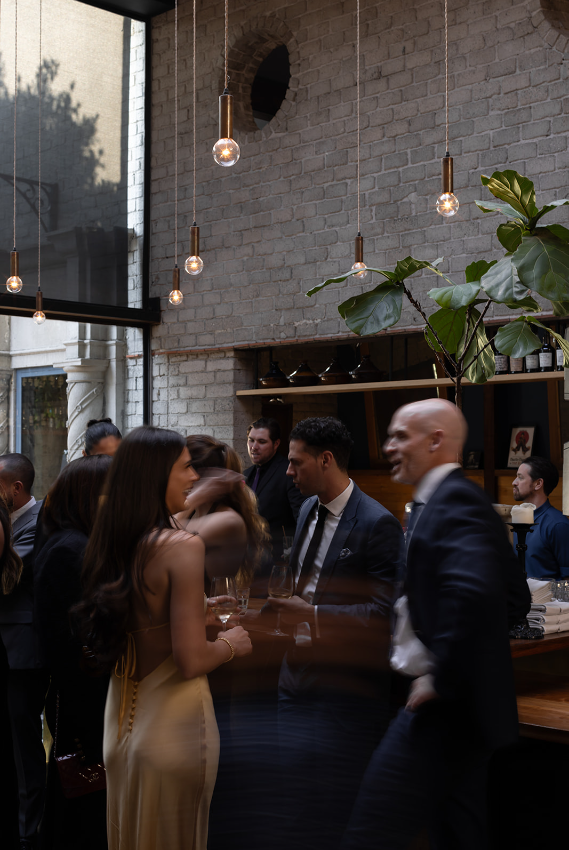 Cocktail reception with well-dressed guests mingling in industrial brick space with hanging Edison bulbs