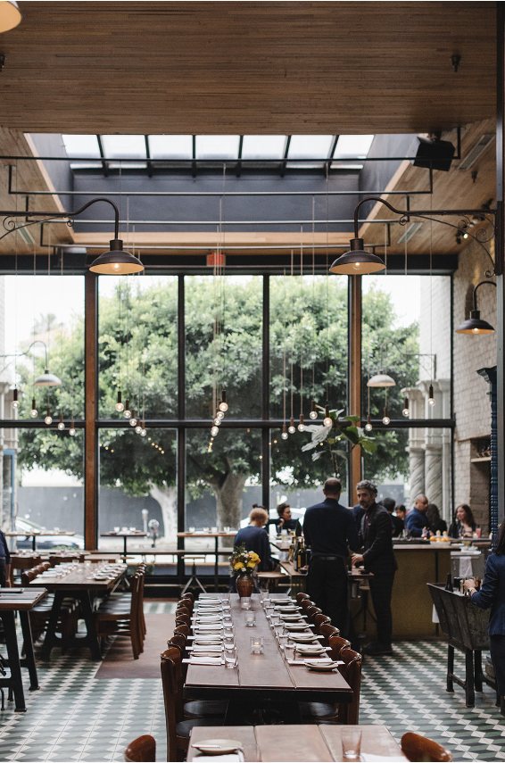 Front dining room with floor-to-ceiling windows, large skylight, decorative tile floors, and long tables set for daytime service