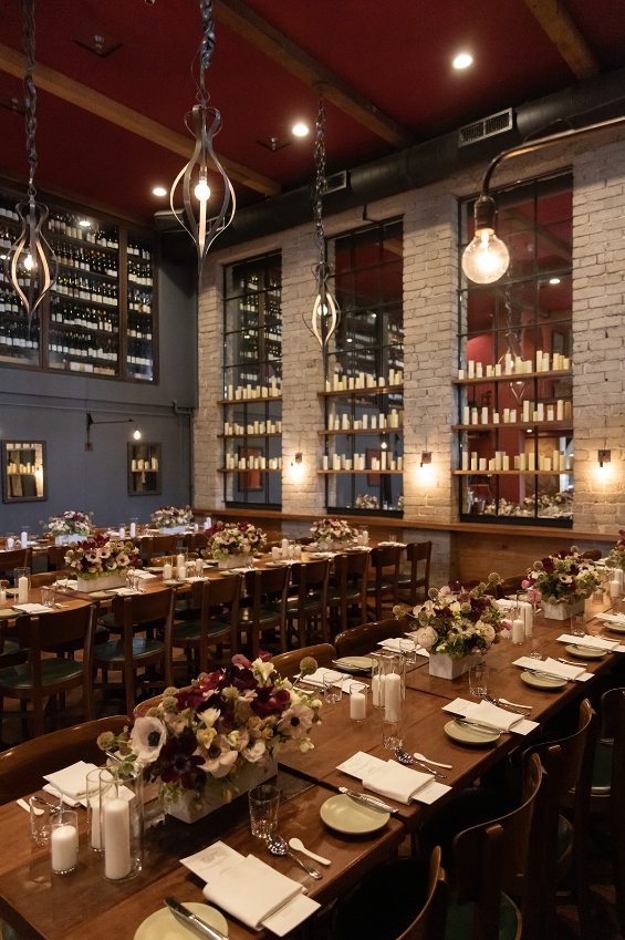 Evening dining setup with wine storage walls, pendant lights, and long tables decorated with floral arrangements