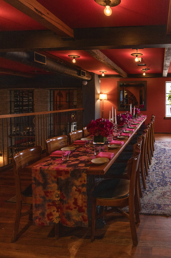 Dining room with red wall and ceiling, exposed beams, long table with floral runner set for formal event
