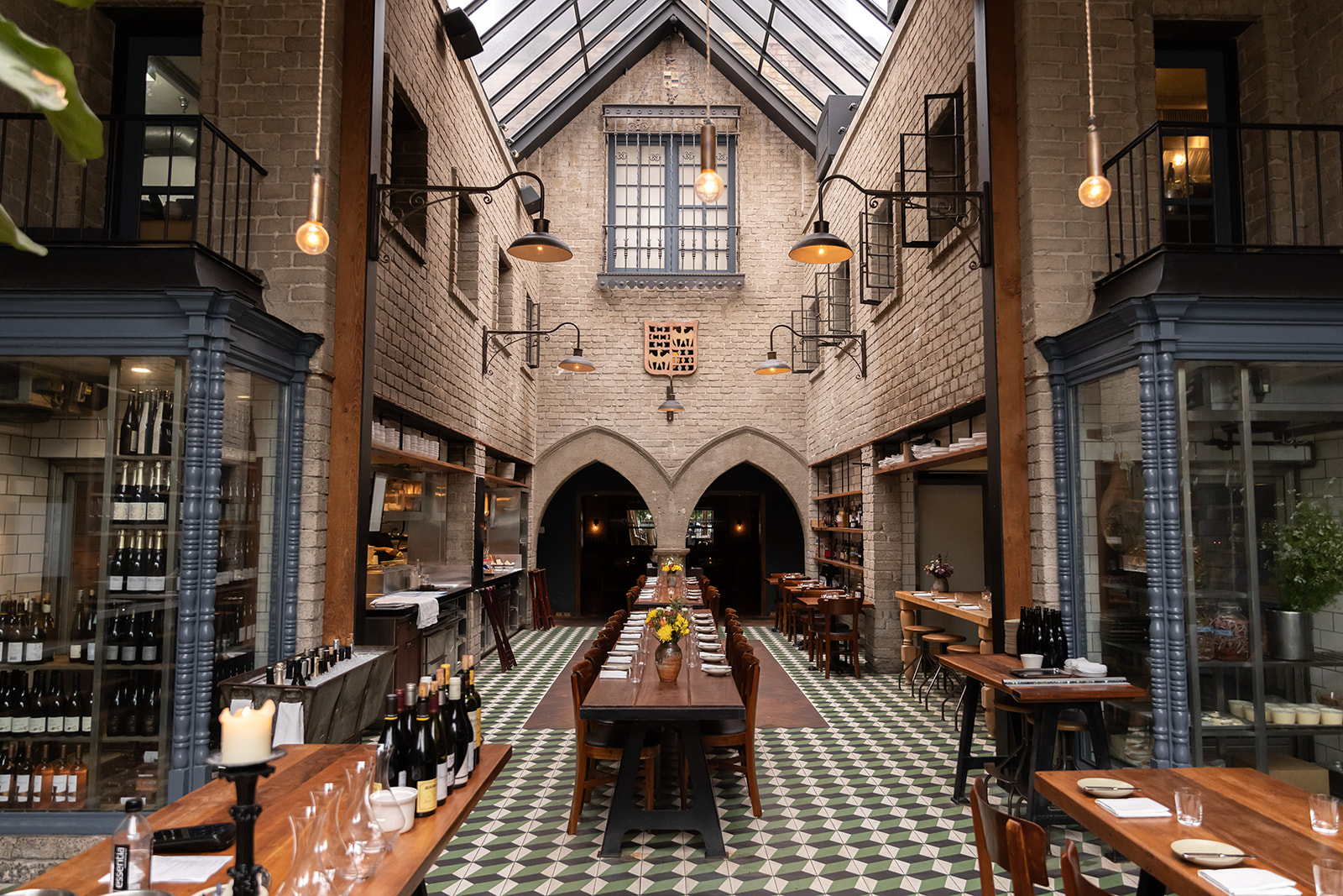 Grand dining hall with vaulted skylight ceiling, gothic arches, checkered green tile floors, and long wooden tables set for service